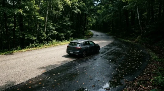Voiture sur route humide traversant une zone ombragée en forêt avec reflets brillants sur la chaussée