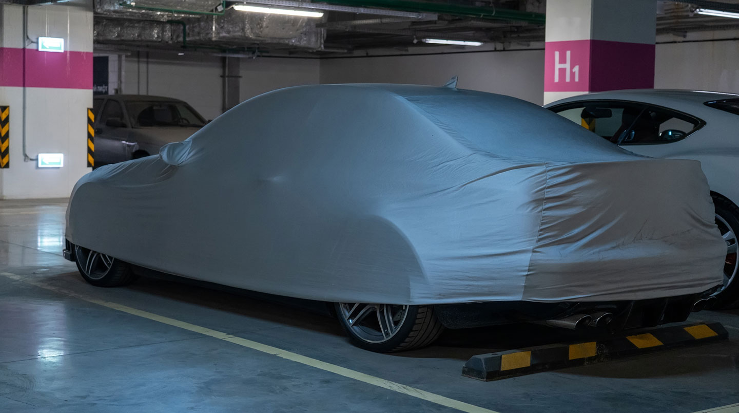 Voiture stationnée dans une allée de maison résidentielle, légèrement poussiéreuse, avec un garage visible en arrière-plan sous un ciel couvert