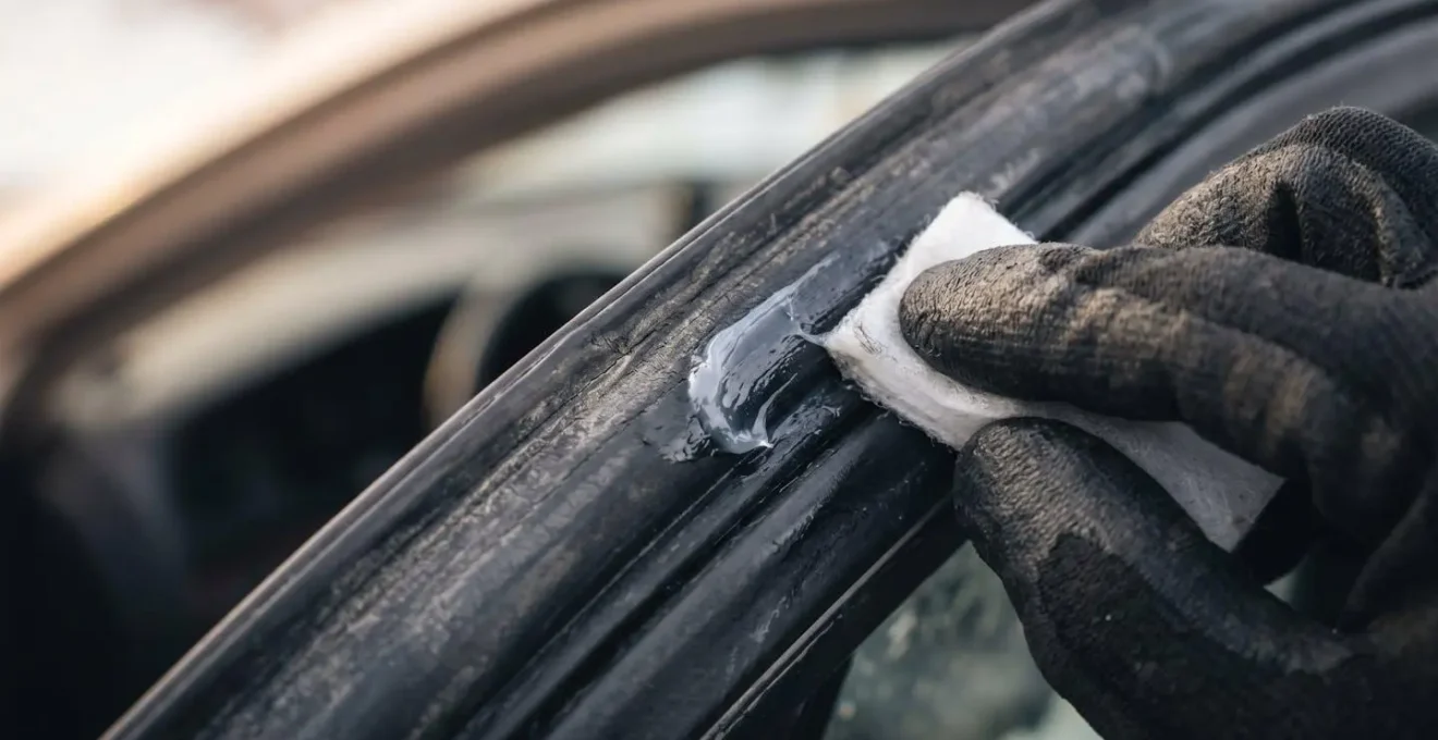 Main appliquant de la graisse silicone sur le joint de portière noir d'une voiture.
